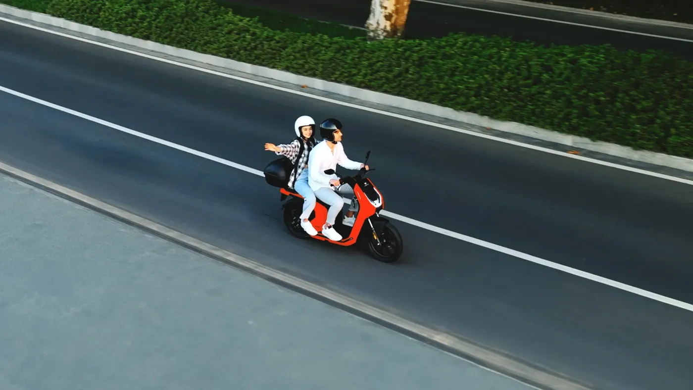 Deux personnes portant un casque sur un scooter électrique VMoto rouge et blanc, en illustration de l’autonomie en déplacement.