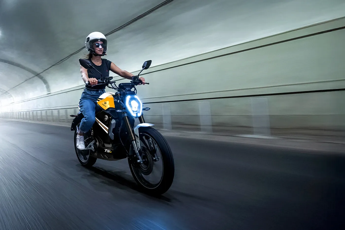 Conductrice casquée sur un deux-roues électrique VMoto TSX jaune dans un tunnel, pour illustrer les trajets urbains quotidiens.